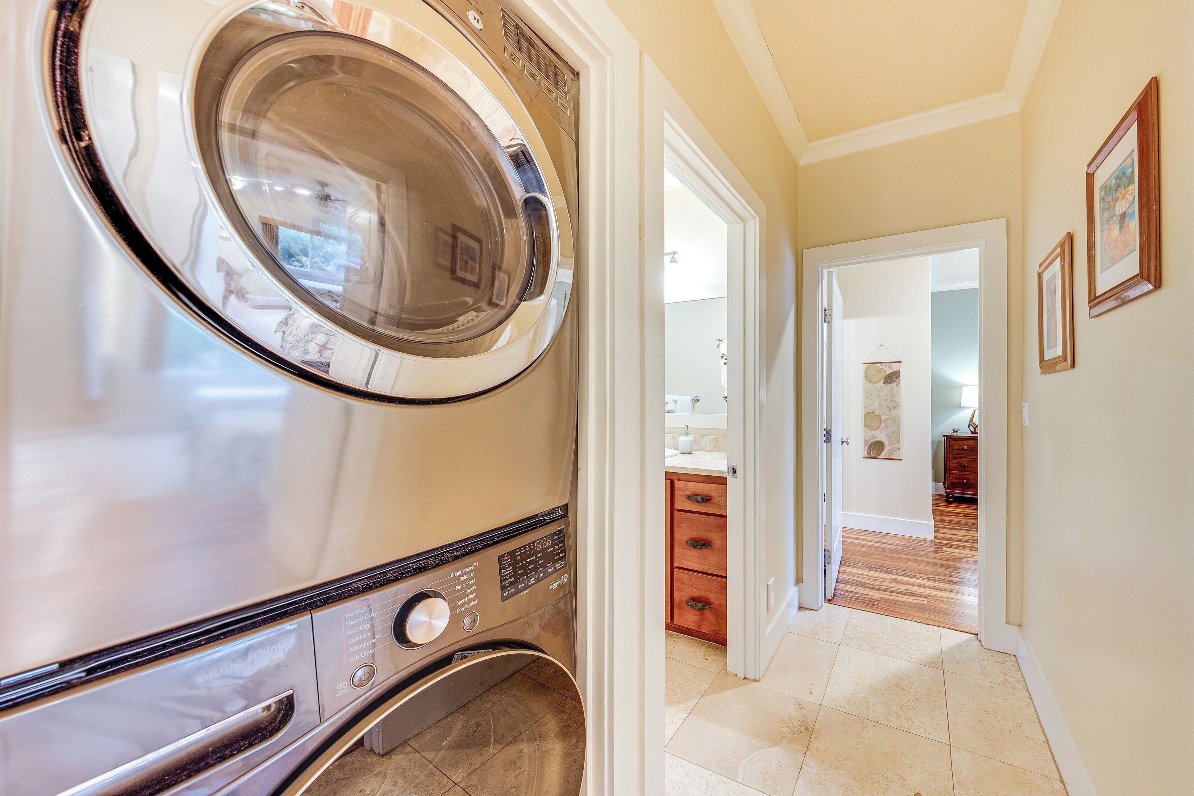 A compact, modern laundry room with a front-loading washer and dryer, a wooden cabinet, and a hallway leading to a bathroom.