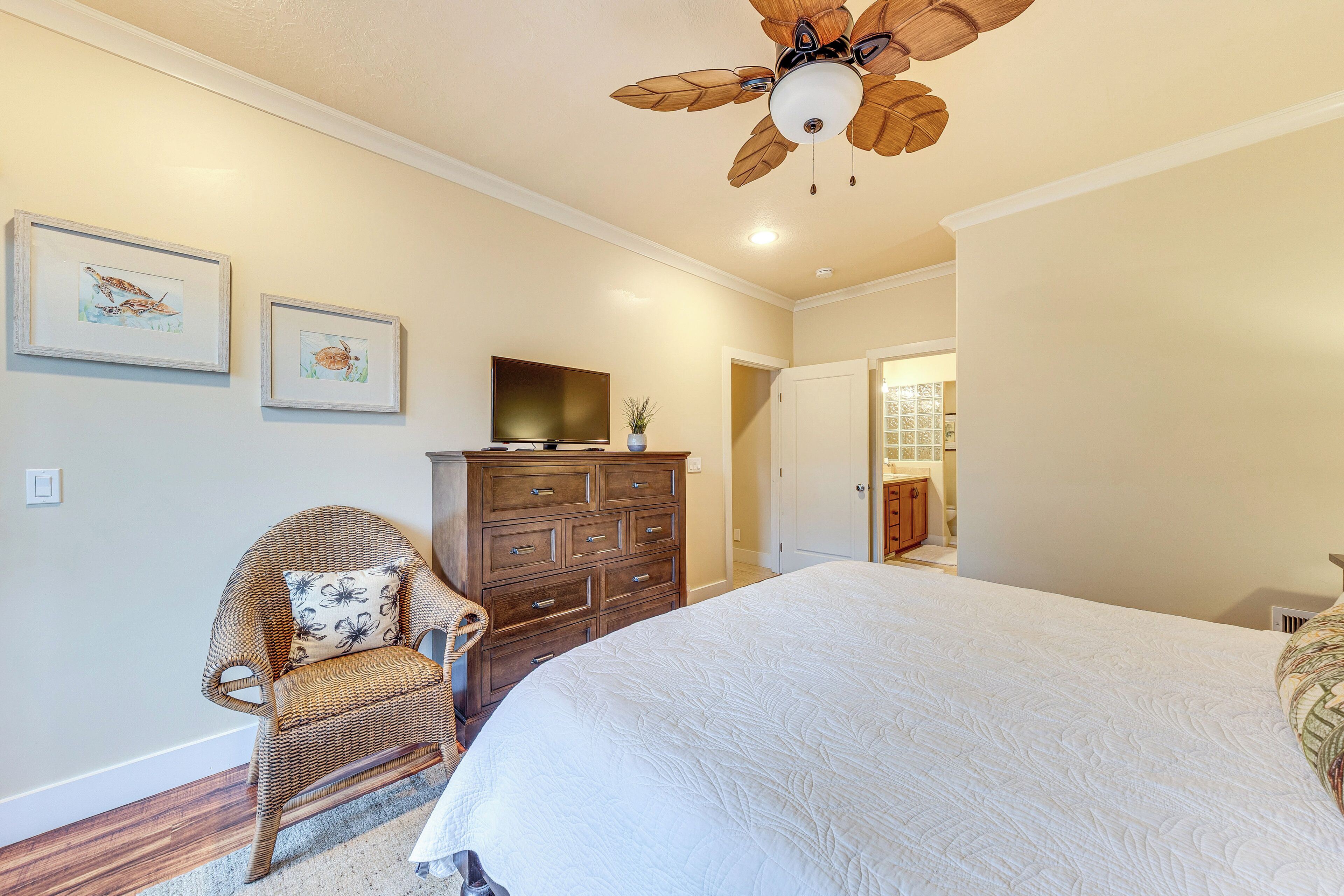 Une chambre à coucher avec un grand lit, une commode en bois, un fauteuil en osier et un ventilateur de plafond.