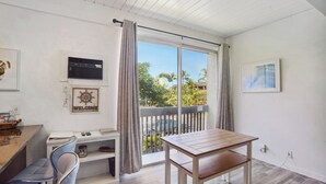 A room with a wooden table and chairs, a small desk with a computer, a window with curtains, and a view of palm trees and a car outside. - < 1 Mi to Beach + Town! Airy Kailua-kona Condo (Kailua-Kona)