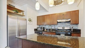 A modern kitchen with wooden cabinets, stainless steel appliances, and a granite countertop. - < 1 Mi to Beach + Town! Airy Kailua-kona Condo (Kailua-Kona)