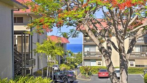 A residential area with multi-story buildings, a parking lot, and a tree with red flowers. - < 1 Mi to Beach + Town! Airy Kailua-kona Condo (Kailua-Kona)