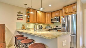 A kitchen with wooden cabinets, a stainless steel refrigerator, a microwave, and a granite countertop.