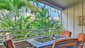 A balcony with a table and chairs, surrounded by lush green plants and a clear view of the sky.