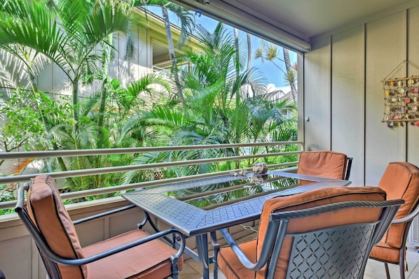 Un balcon avec une table et des chaises, entouré d’une végétation luxuriante et offrant une vue sur les bâtiments.
