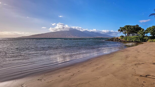 A beach with a mountain in the background, clear skies, and calm water.