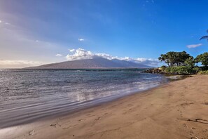 A beach with a mountain in the background, clear skies, and calm water. - Kihei Condo: Steps to Kalepolepo Beach Park! (Kihei)