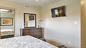 Un dormitorio con cama, cómoda, espejo, ventilador de techo y televisor.