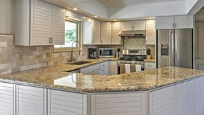 Una cocina moderna con encimeras de granito, electrodomésticos de acero inoxidable y armarios blancos.