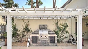 Un área de barbacoa al aire libre con una parrilla de piedra, un pérgola arriba y vistas del jardín circundante.
