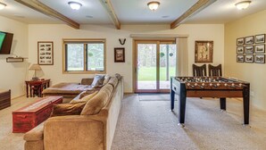 A cozy living room with a sofa, a foosball table, and a television. - Scenic Forest Lodge Outside Glacier National Park! (West Glacier)