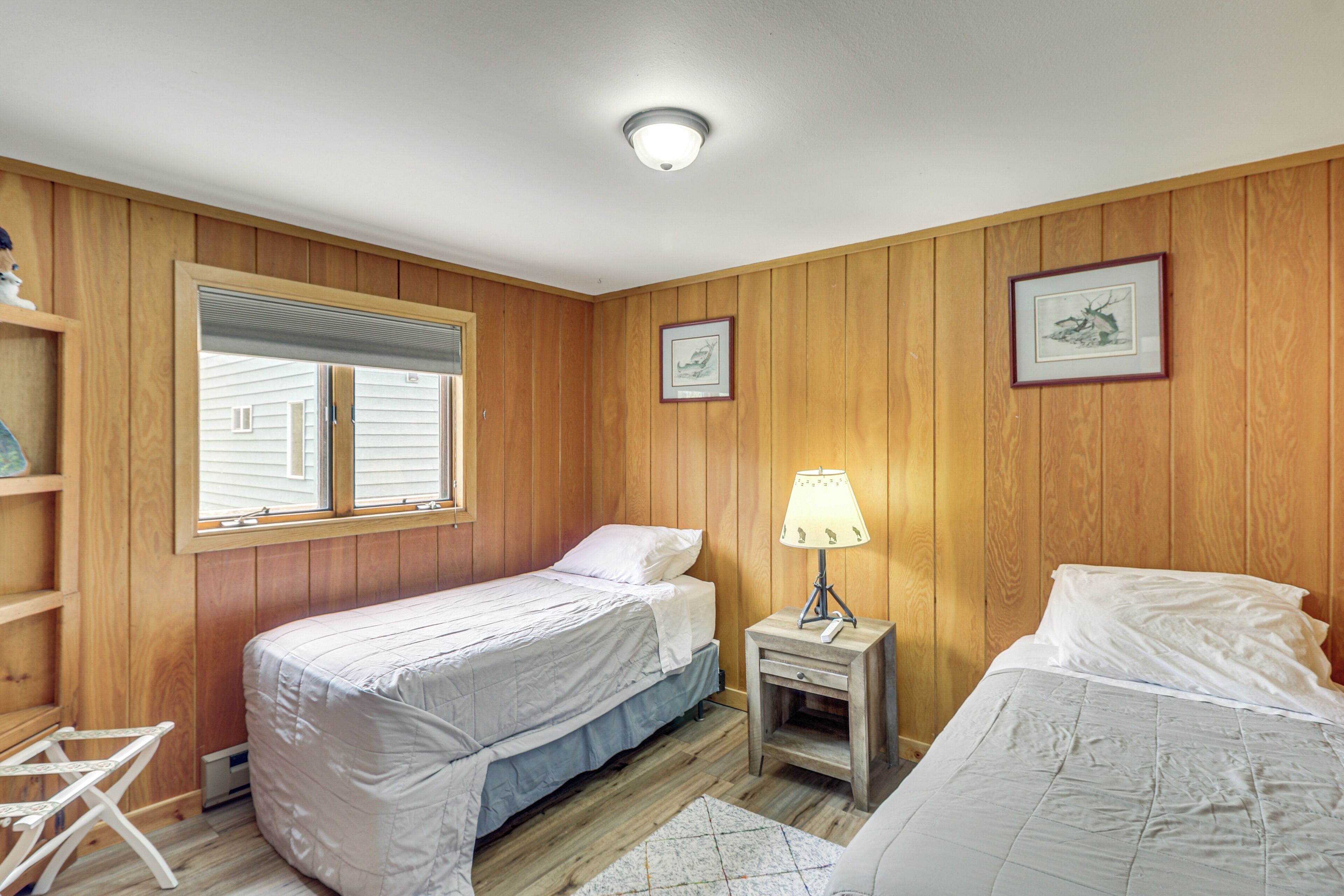 A room with two beds, wooden walls, a window, and a lamp.