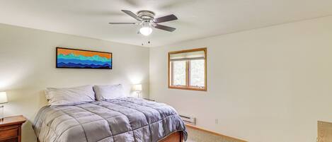 A bedroom with a bed, a ceiling fan, a window, and a painting on the wall.