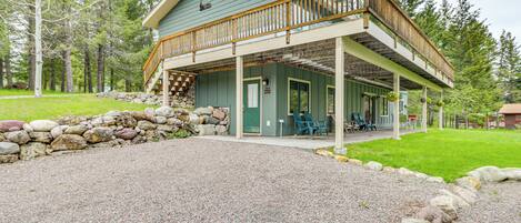 A two-story cabin with a balcony, stone wall, and a gravel driveway.