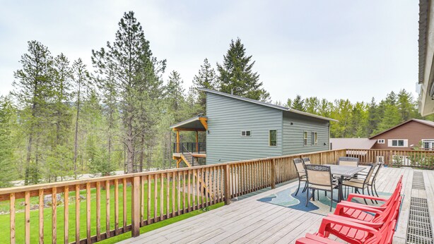 A wooden deck with outdoor furniture, a small building, and a view of a forested area. - Scenic Forest Lodge Outside Glacier National Park! (West Glacier)