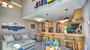 A modern living room with a sofa, coffee table, and chairs, a kitchen area with wooden cabinets and a bar, and artwork on the walls. - Ski-in/ski-out Lutsen Retreat w/ Pool Access! (Lutsen)