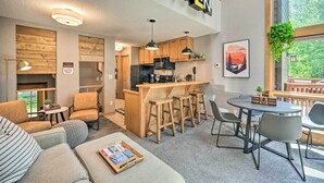 A modern kitchen with wooden cabinets, a central island with stools, and a dining area with a round table and chairs. - Ski-in/ski-out Lutsen Retreat w/ Pool Access! (Lutsen)