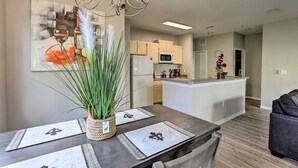 Una cocina moderna con una isla central, una mesa de comedor con individuales, una araña y una planta en maceta.