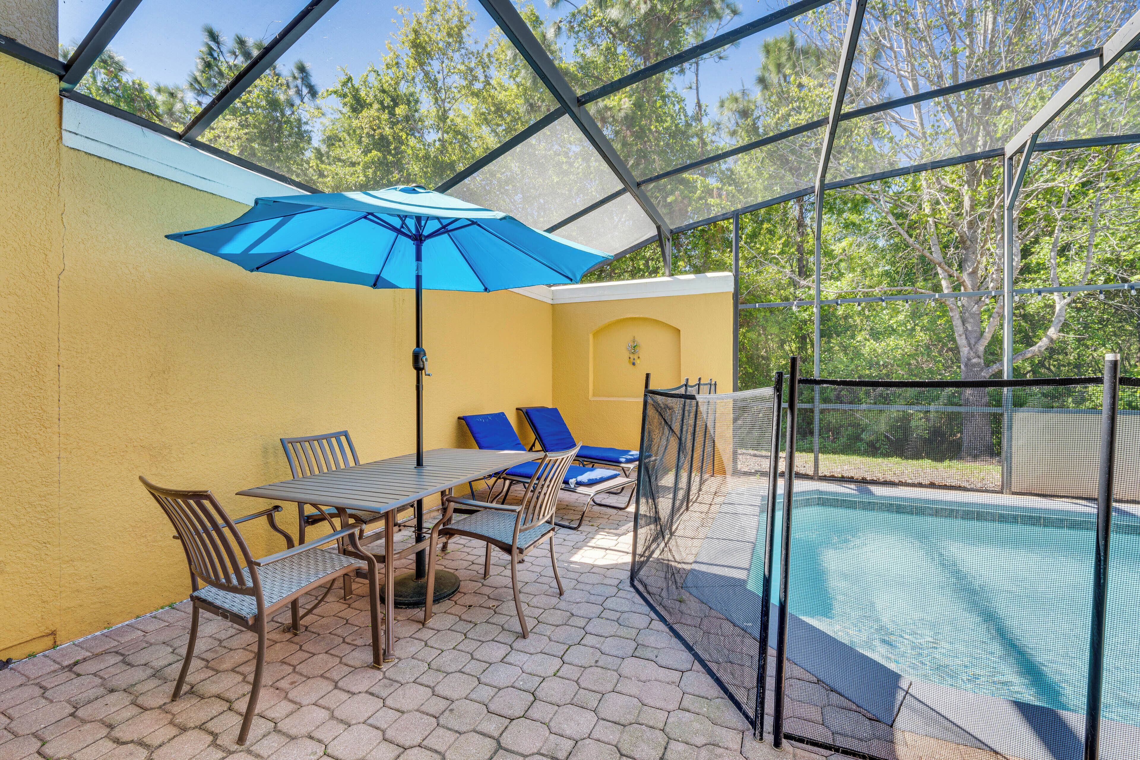 Alpendre coberto com piscina, móveis de exterior e um guarda-sol azul.