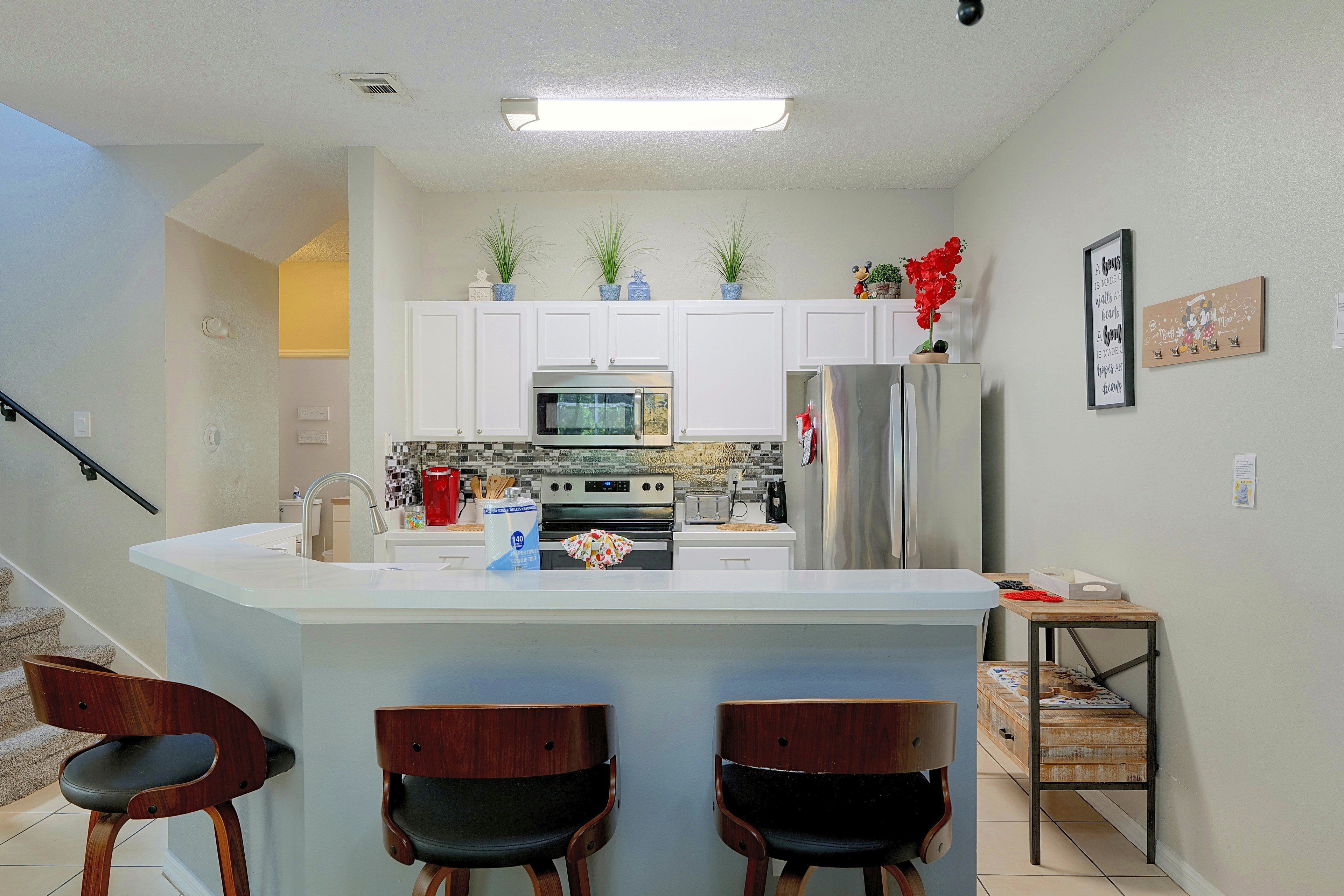 A modern kitchen with white cabinets, a central island with bar stools, a stainless steel refrigerator, and a microwave.