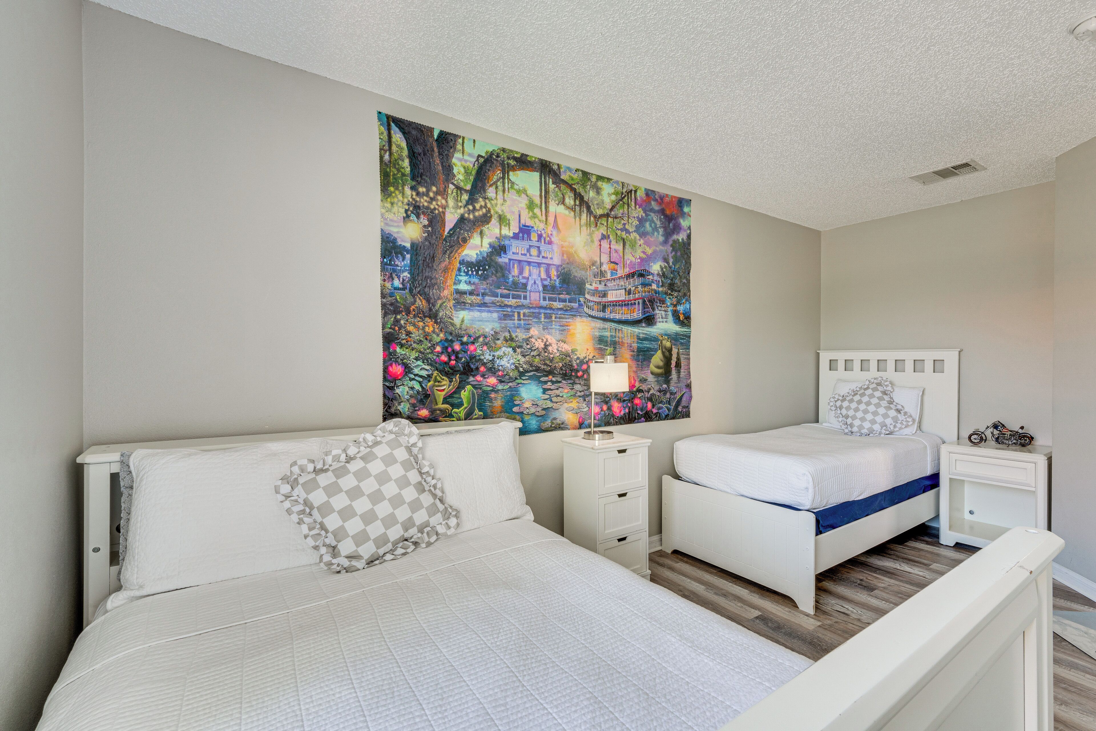Une chambre à coucher avec un grand lit, un plus petit lit, une table de chevet et un tableau accroché au mur.