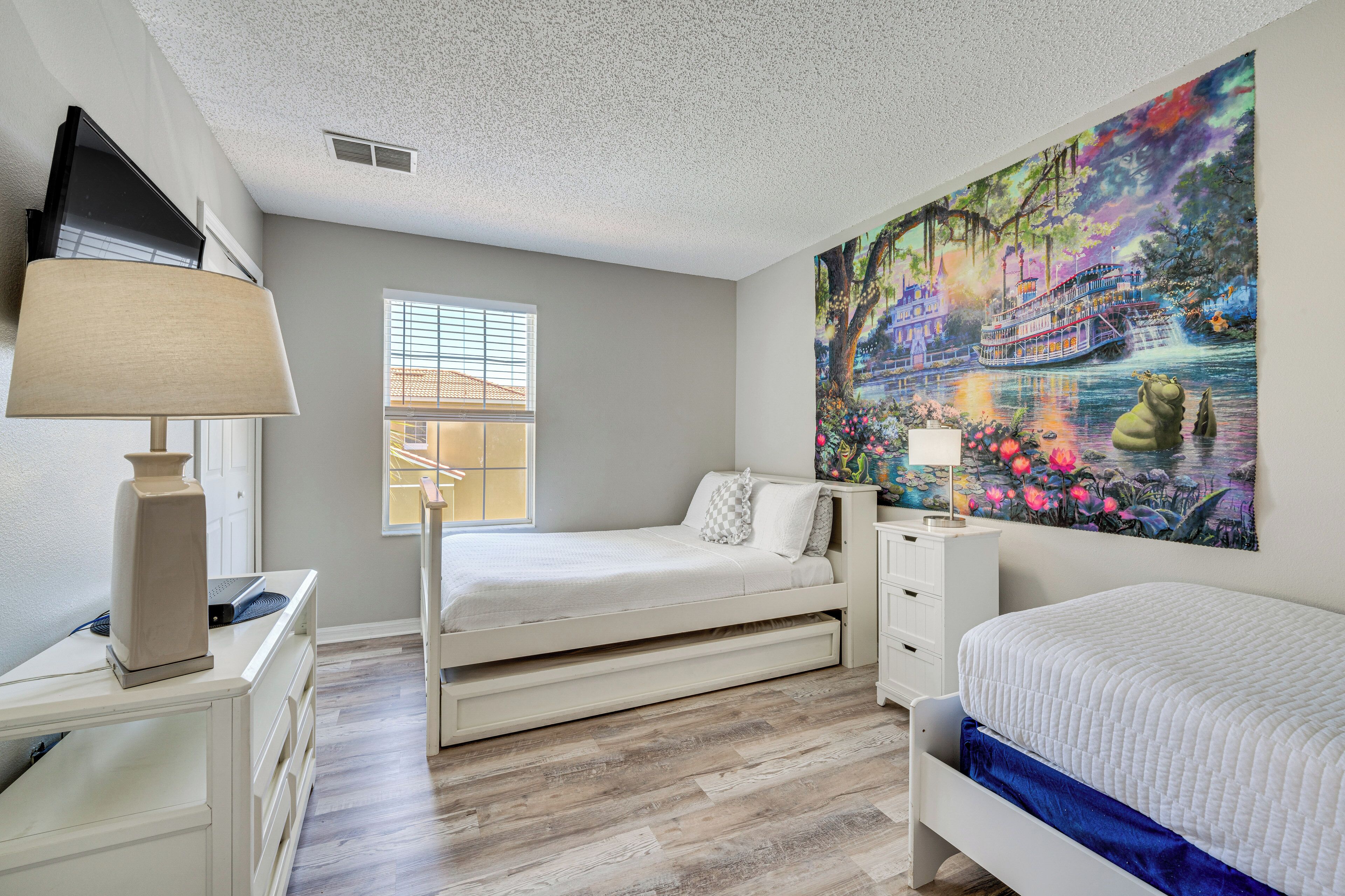 A bedroom with a bed, a desk, a lamp, a window, and a large painting on the wall.