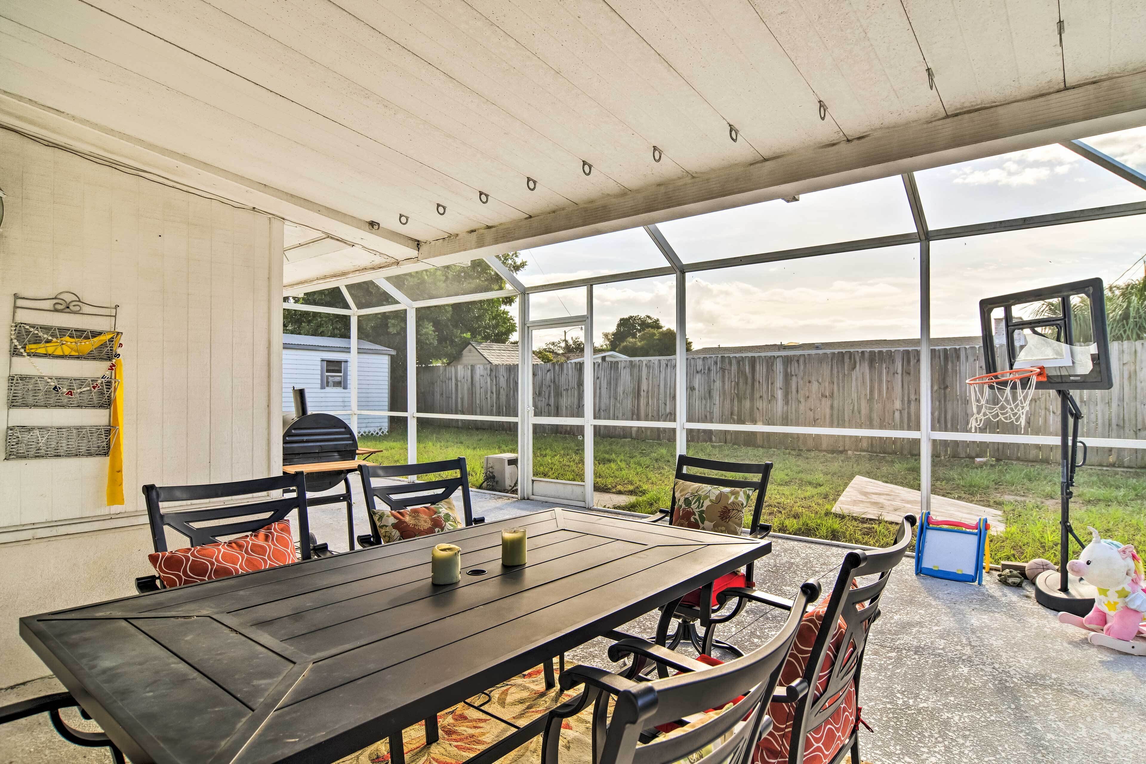 Un patio techado con una mesa y sillas, un aro de baloncesto y vistas a un jardín trasero.