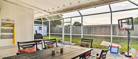 A covered patio with a table and chairs, a basketball hoop, and a view of a backyard.