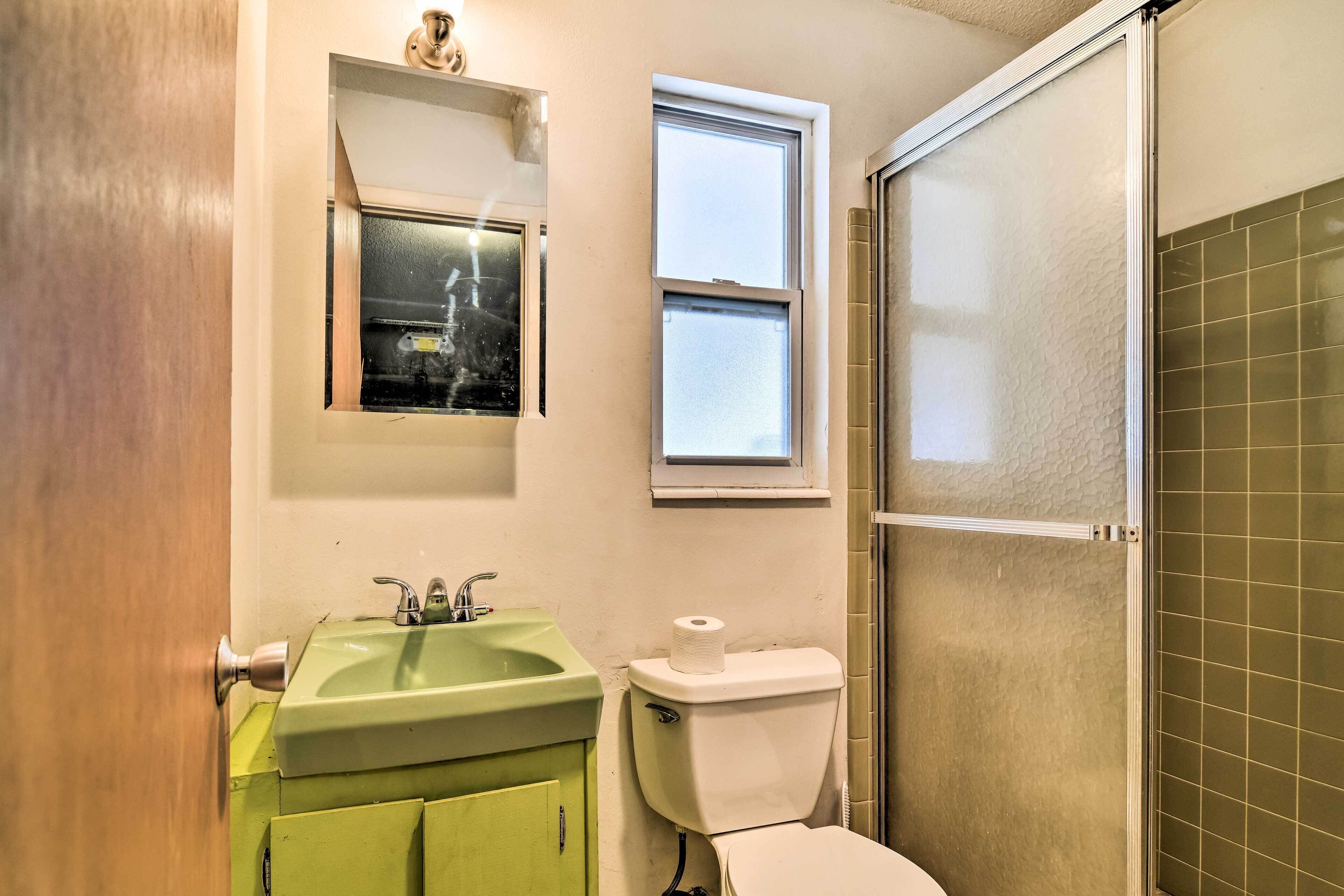Un baño con un lavabo verde, un inodoro, una ventana y una zona de ducha.