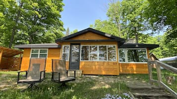 Relax on the cabin's porch with two chairs and a small table amidst lush greenery.