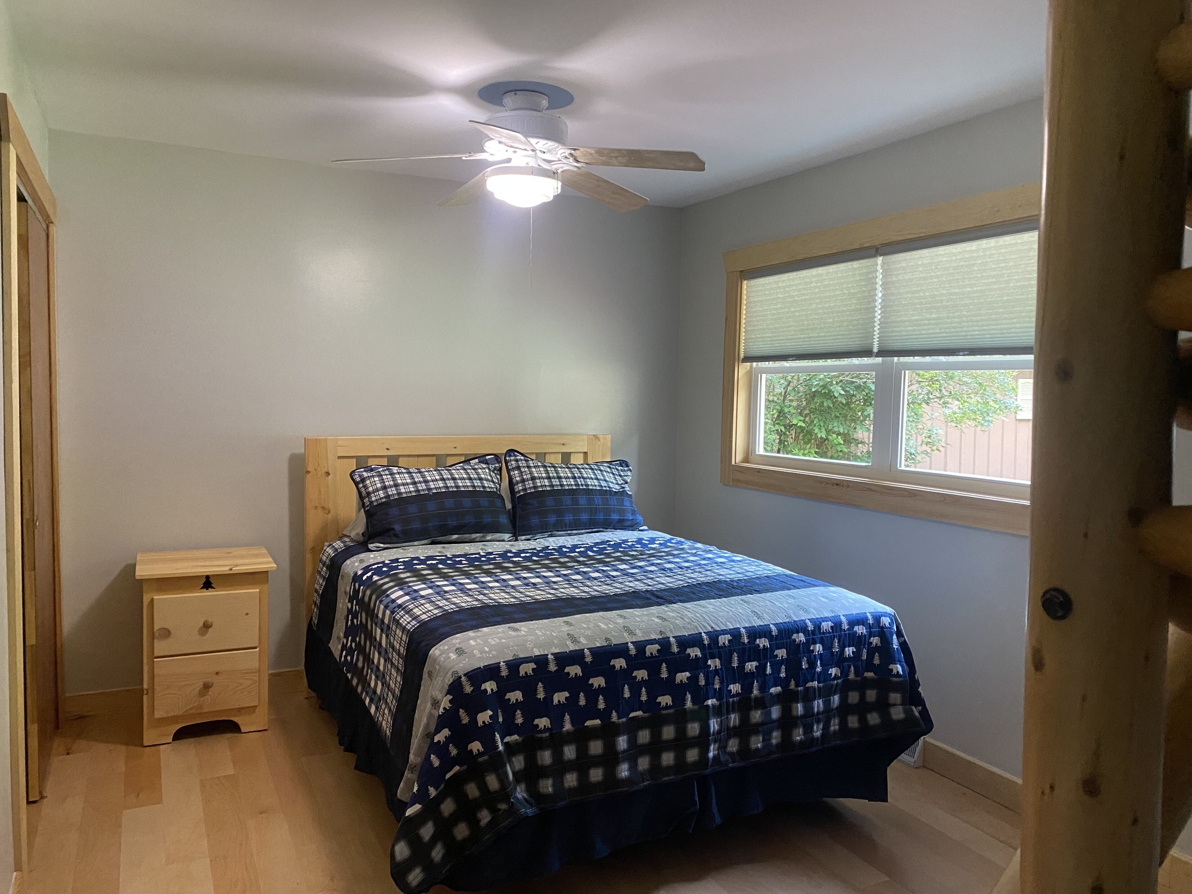 A bedroom with a bed, a nightstand, a ceiling fan, and a window.