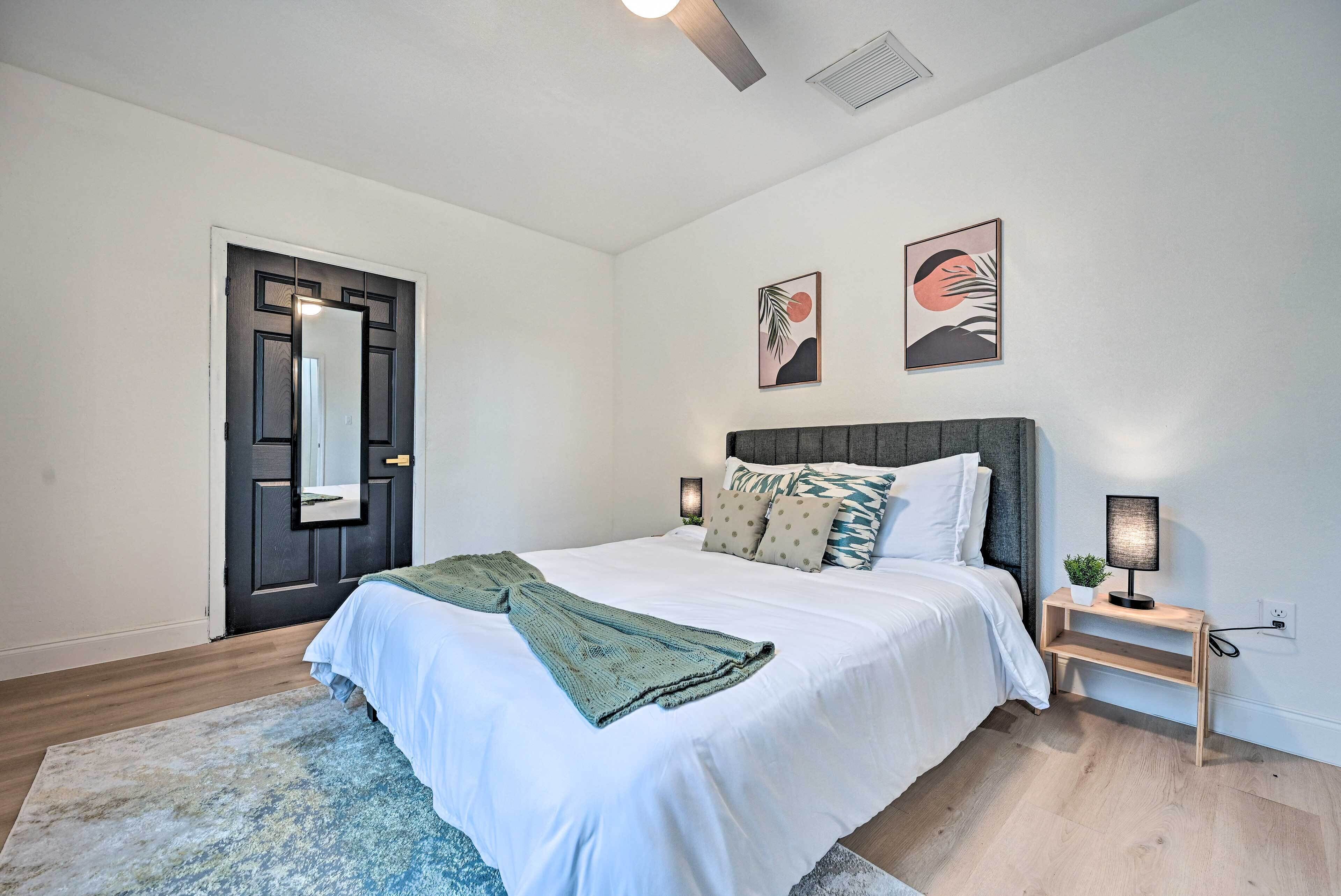 A bedroom with a bed, a nightstand, a mirror, and artwork on the wall.