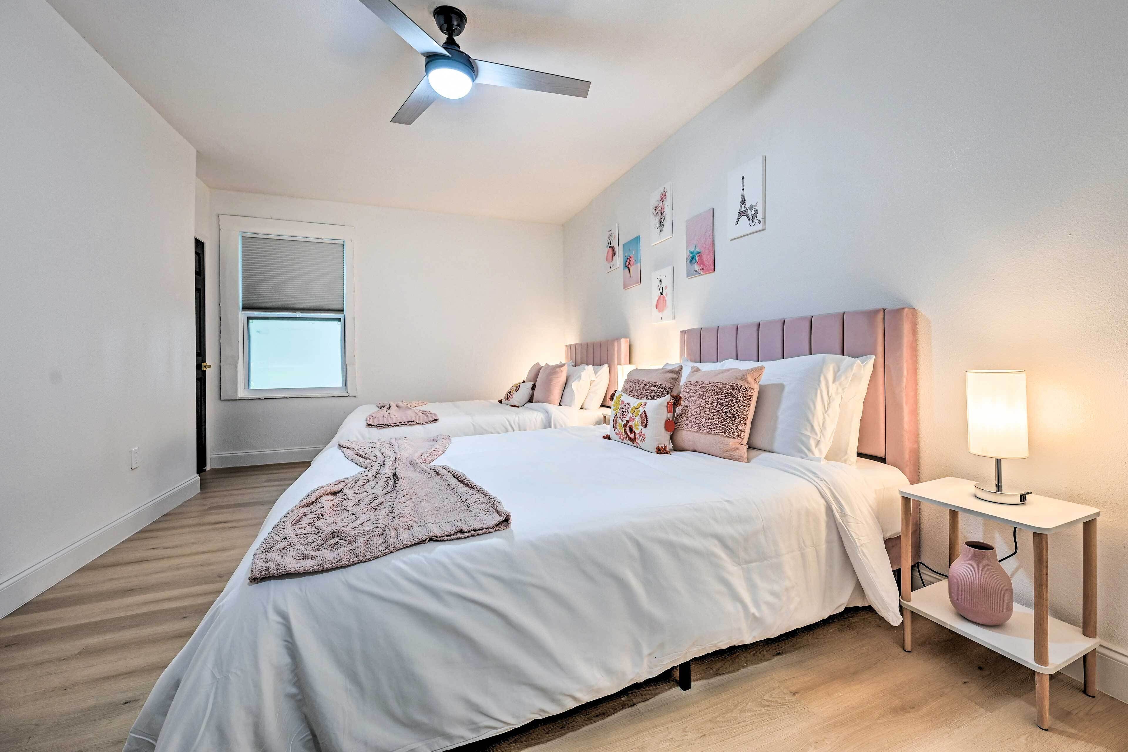 A bedroom with two beds, a ceiling fan, a bedside table with a lamp, and a window with blinds.