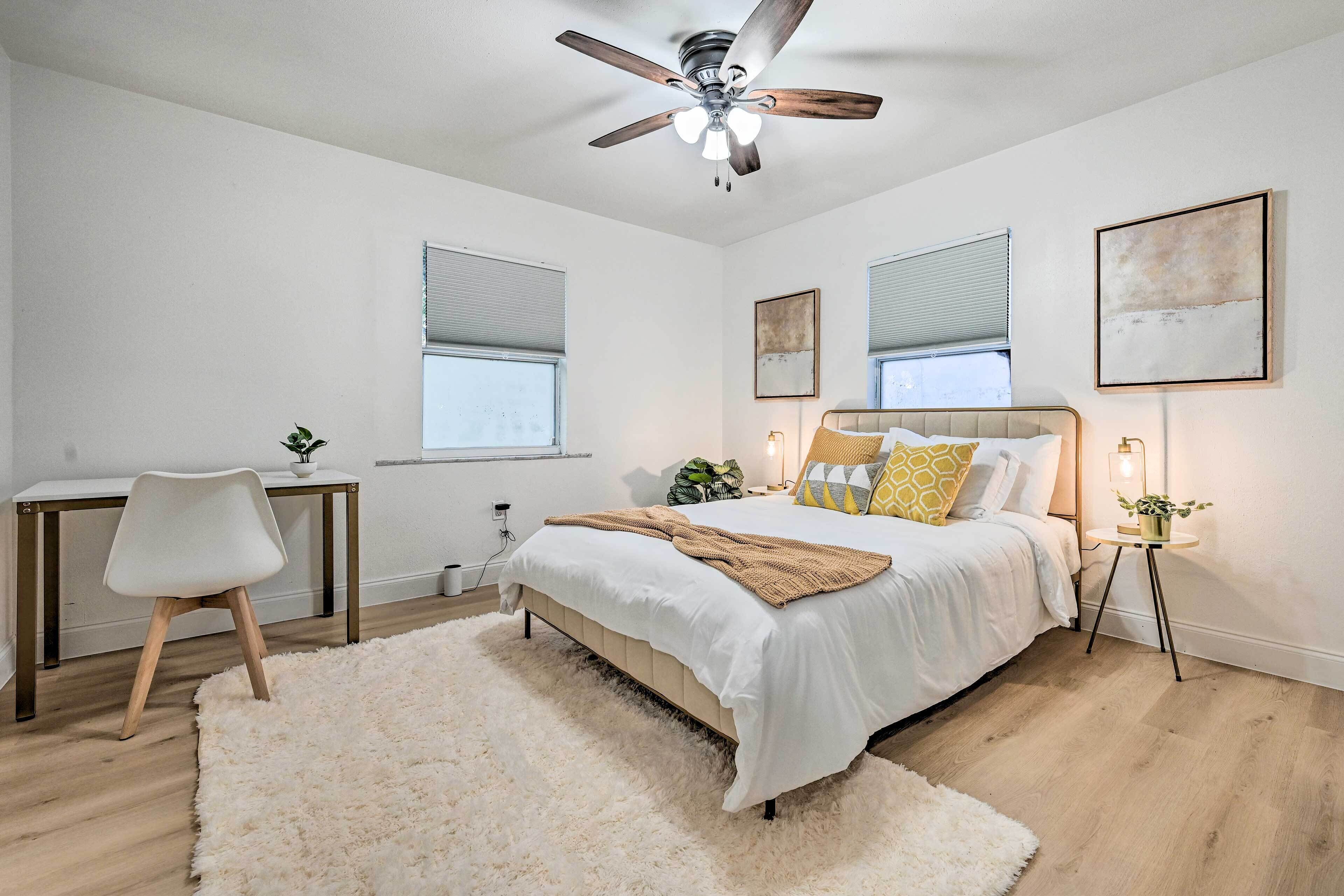 A bedroom with a bed, a desk, a chair, a ceiling fan, and a window.