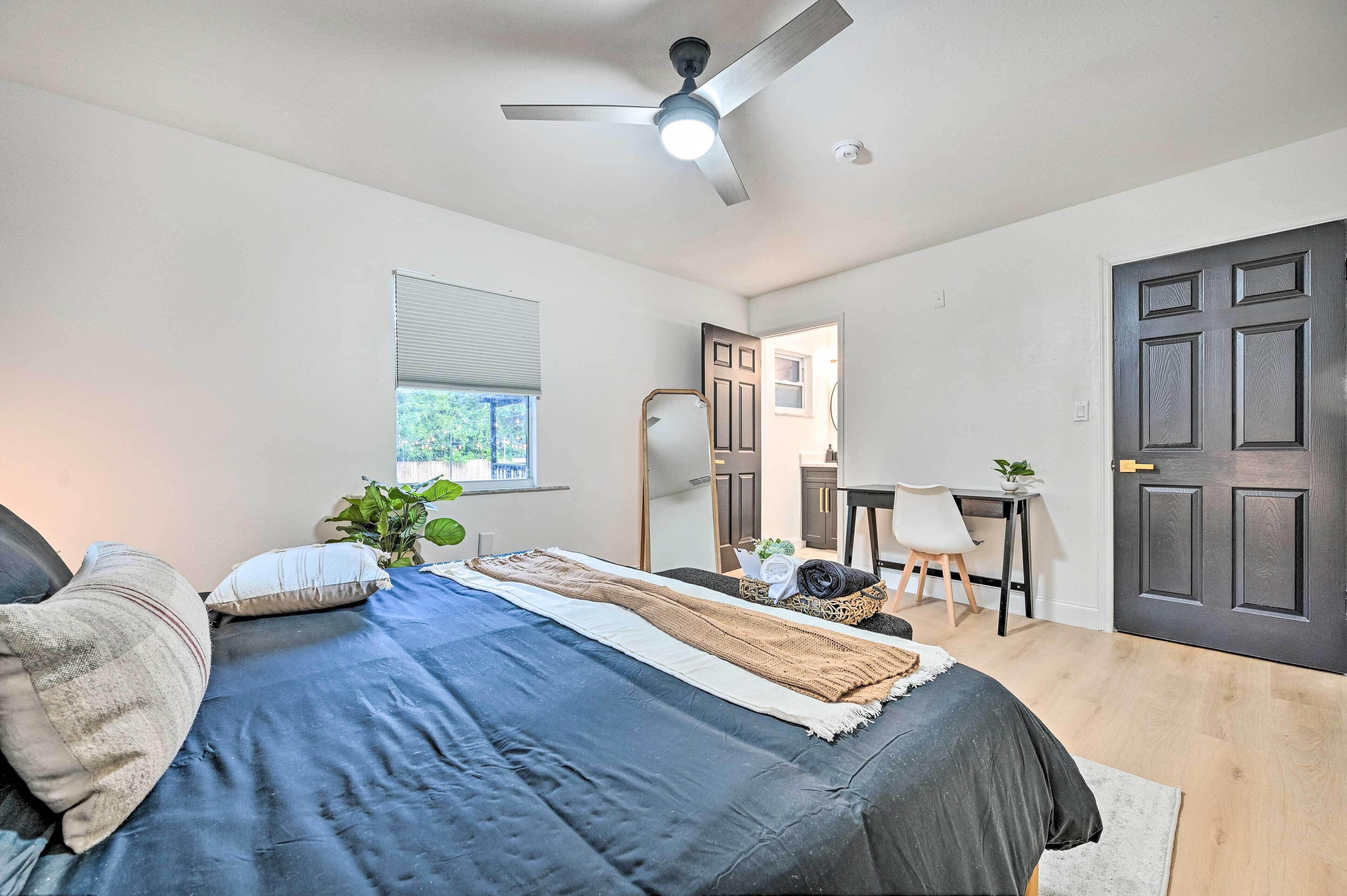 A bedroom with a bed, a ceiling fan, a window, a desk, and a door.