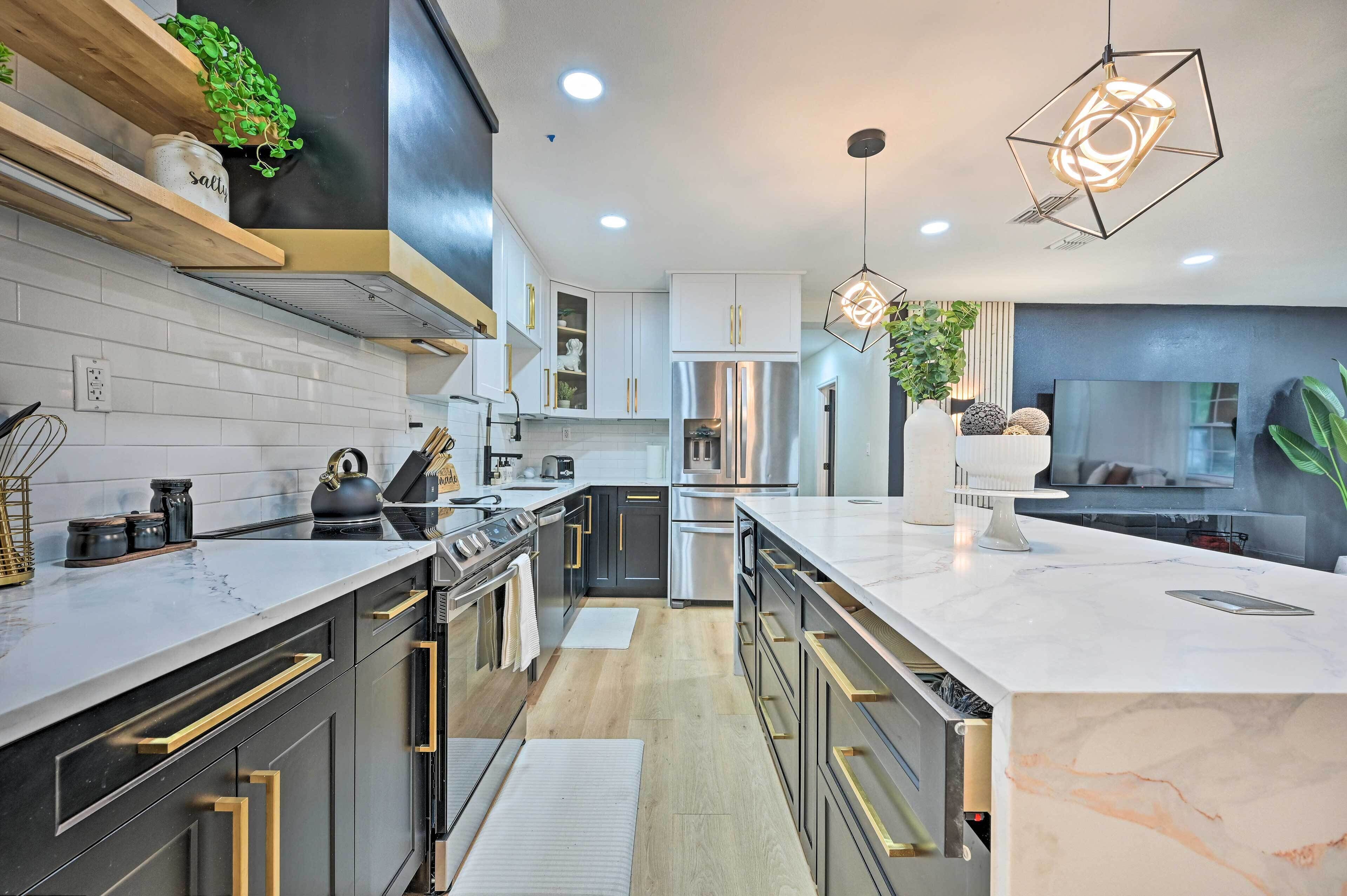 A modern kitchen with stainless steel appliances, wooden shelves, and a marble countertop.