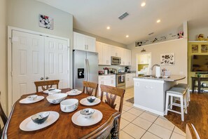 A modern kitchen with white cabinets, a central island, and a dining area with a wooden table and chairs.