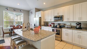 A kitchen with white cabinets, a granite countertop, a stainless steel refrigerator, a microwave, a stove, and a coffee maker. - Pool, Themed Rooms & Arcade: Disney Escape (Kissimmee)