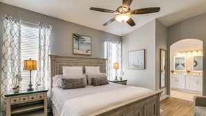 A bedroom with a bed, nightstands, a ceiling fan, and a bathroom with a vanity and mirror. - Pool, Themed Rooms & Arcade: Disney Escape (Kissimmee)
