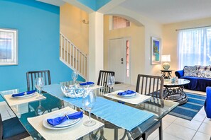 A dining area with a glass table set for six, a staircase, a living room with a sofa, and a door leading to another room.
