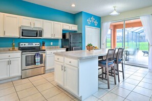 A kitchen with white cabinets, a stainless steel oven, a microwave, and a refrigerator. There is a large island with chairs and a potted plant.