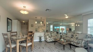 A spacious living room with a dining area, a large mirror, and a kitchen in the background.