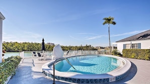 A swimming pool with a 3 FT depth marker, surrounded by a deck with chairs and a covered area, overlooking a body of water and palm trees.
