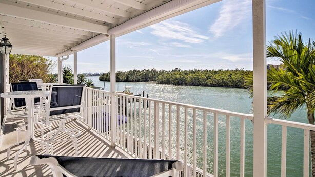 A covered outdoor deck with white railings, seating, and a view of a river and greenery.