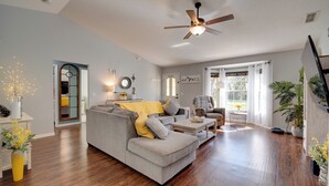 Un salon spacieux avec un canapé d’angle gris, un ventilateur de plafond et un plancher en bois.