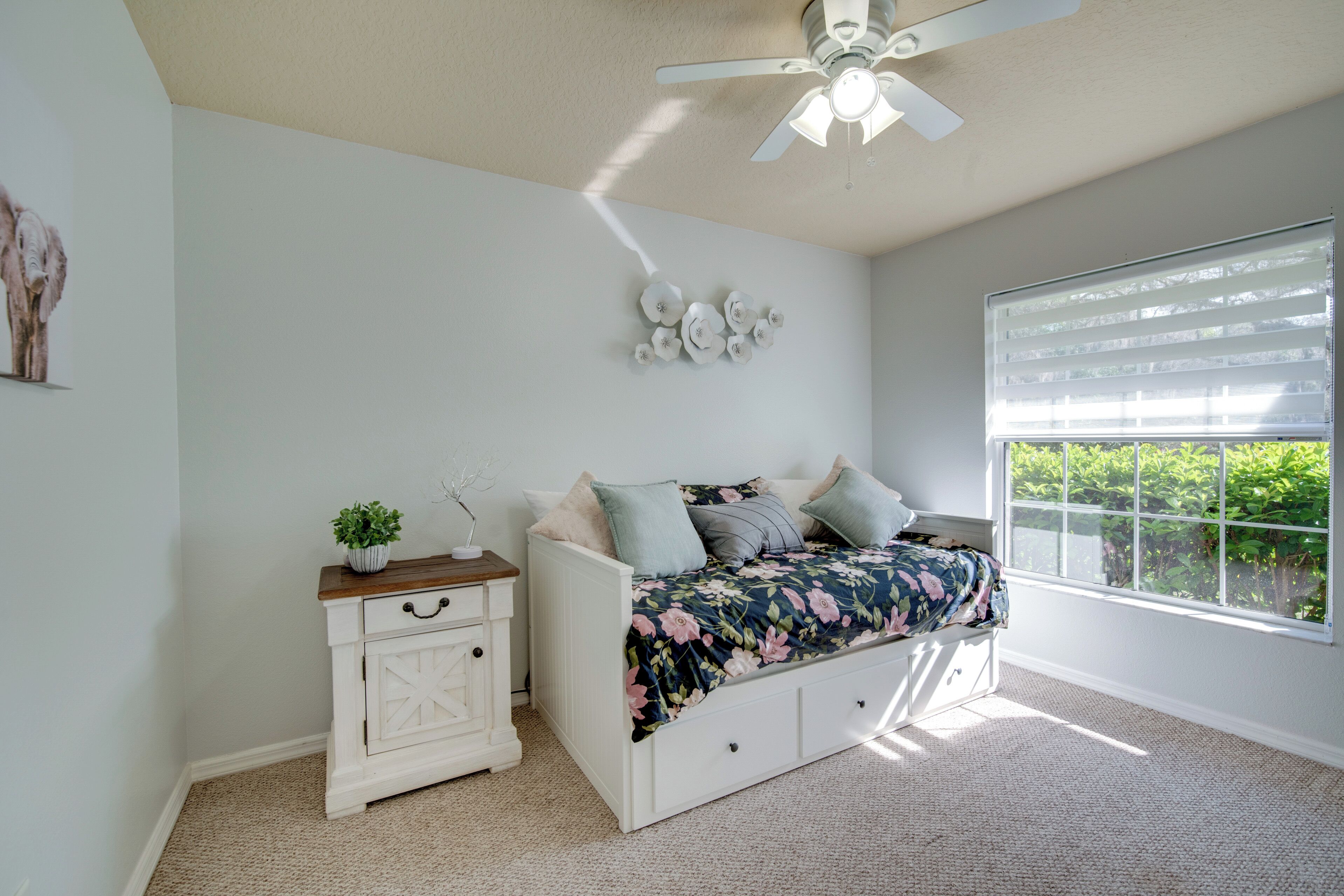 A bedroom with a bed, a nightstand, a ceiling fan, and a window with blinds.