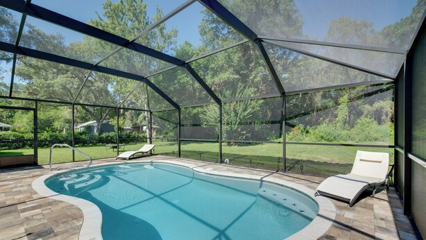 Une piscine couverte à la forme incurvée, entourée de chaises longues et d’un espace patio.