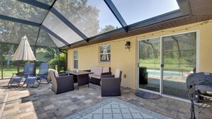 Un patio couvert aménagé avec du mobilier d’extérieur, un barbecue et une vue sur une piscine.