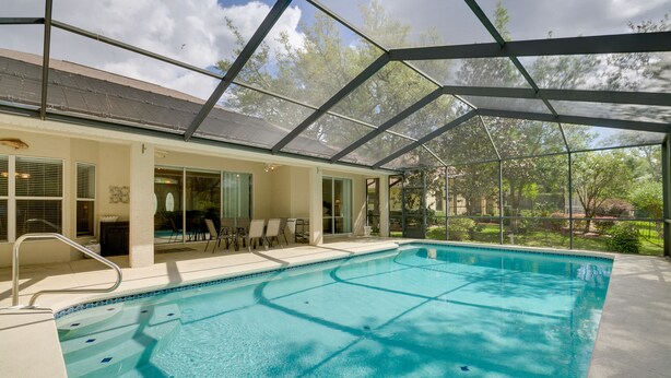 Ein Schwimmbad mit Glasveranda, umgeben von einer Terrasse mit Stühlen und einem Tisch.
