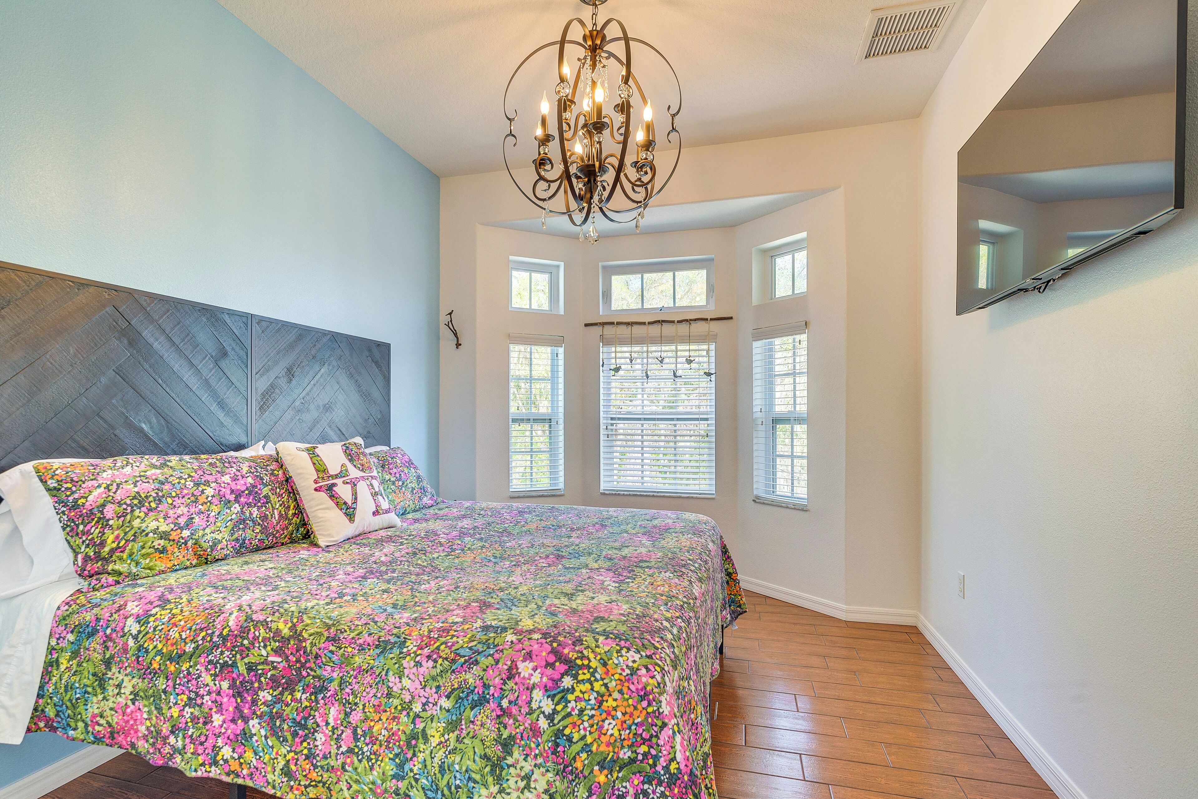 A bedroom with a large bed, a chandelier, and multiple windows.