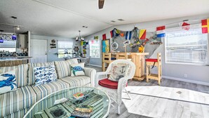 A living room with a striped sofa, a glass coffee table, a white wicker chair, and a ceiling fan. - Elevated Deck! Fun-filled Homosassa River Home (Homosassa)